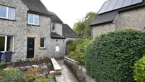 A stone building with a black door and windows, a pathway, and a hedge. - Recently renovated 2 bedroom annexe with open plan living room and kitchen. (Stoney Middleton)