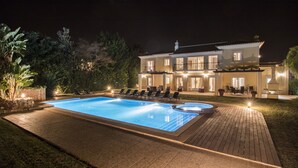 En stor swimmingpool med liggestole og et godt oplyst terrassemiljø.
