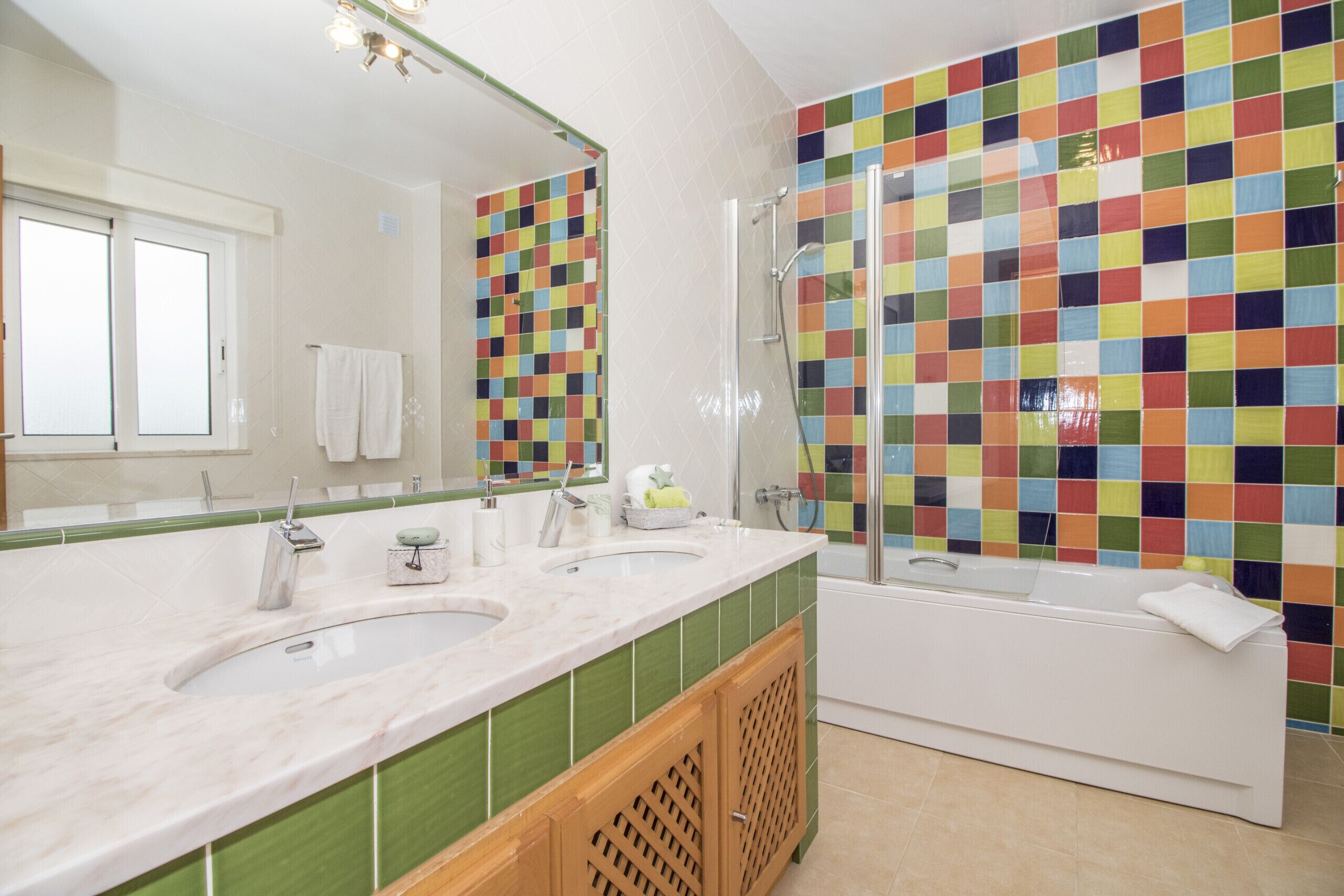 Une salle de bain avec deux lavabos, une baignoire et un mur décoré d’une mosaïque colorée.