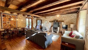 A rustic interior with exposed wooden beams, stone walls, a fireplace, a television, and a dining area with a patterned wall. - Charming, Detached Farmhouse With Private Swimming Pool. (Lizant)
