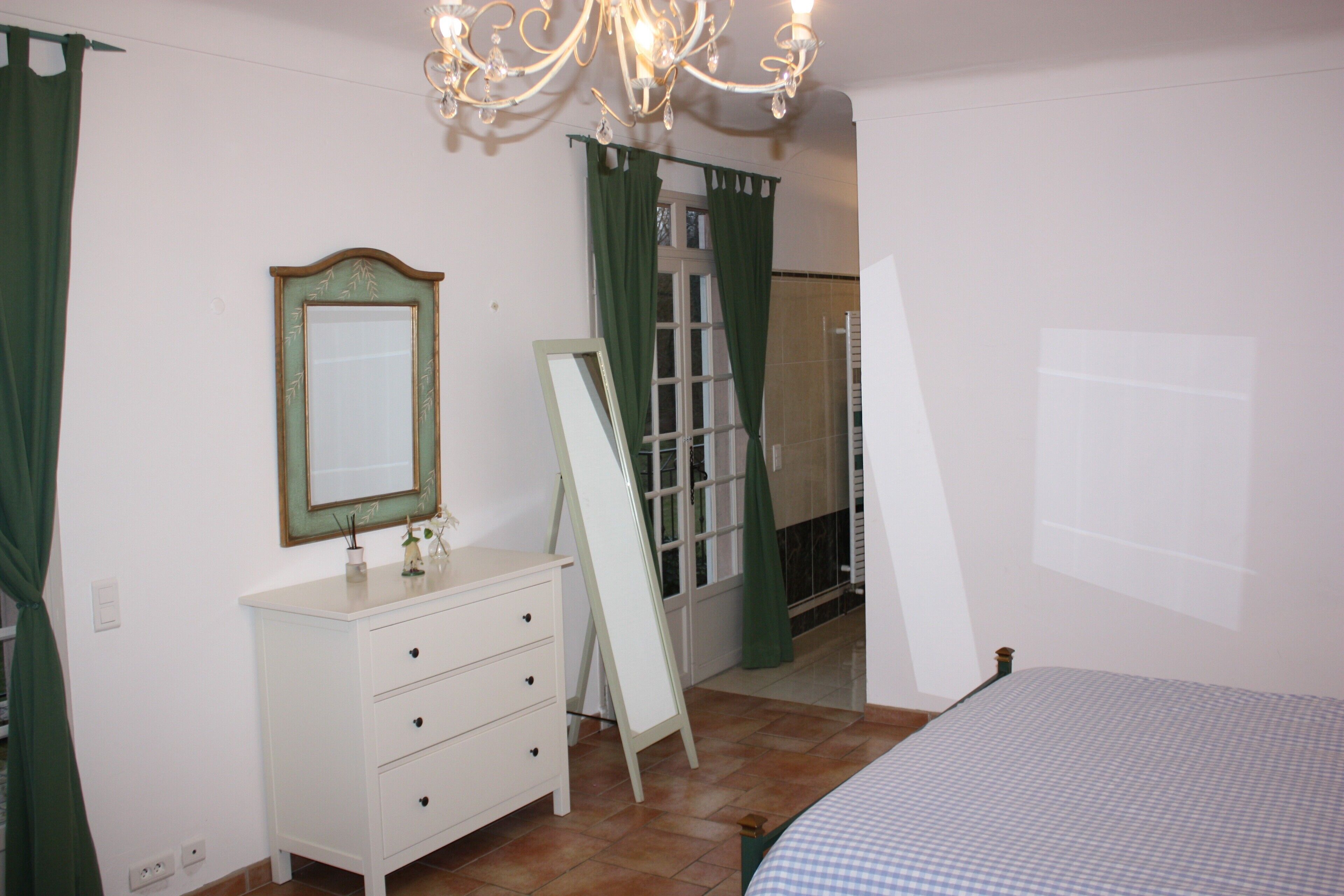 Une chambre à coucher avec un lit, une commode, un miroir et une fenêtre avec des rideaux.