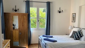 A bedroom with a bed, a wooden wardrobe, a window with curtains, a white rug, and a small rug on the floor. - La Villa Rose is a spacious villa in Provence with a large pool. (Le Thoronet)