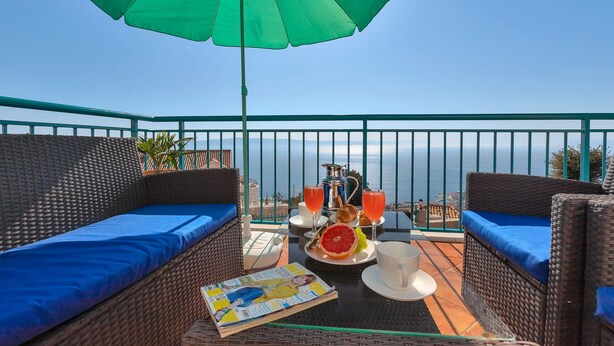 A balcony with wicker furniture, a table with breakfast items, and a view of the sea. - Villa With Large Terrace  (Podgora)