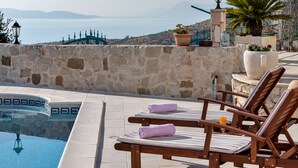 A poolside area with lounge chairs, a stone wall, and a view of the sea. - Villa With Large Terrace  (Podgora)