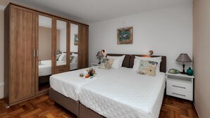 A bedroom with a large wardrobe, a bed with white bedding, a nightstand with a lamp, and a wall clock. - Villa With Large Terrace  (Podgora)