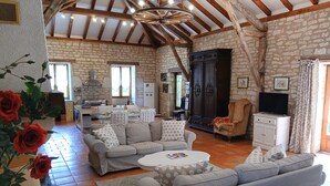 A spacious living area with a stone wall, wooden beams, a sofa set, a television, and a dining area with a kitchen in the background. - Gite Le Sabatou. Converted Barn, Private Pool, 15ha ASPAS Nature Park. (Cézac)