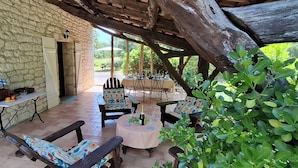 A stone-walled patio with outdoor seating, a table with a bottle and glasses, and a basket with fruits. - Gite Le Sabatou. Converted Barn, Private Pool, 15ha ASPAS Nature Park. (Cézac)