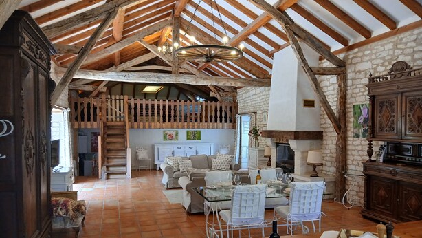 A rustic interior with exposed wooden beams, a stone fireplace, and a dining area with white chairs and a table set for a meal. - Gite Le Sabatou. Converted Barn, Private Pool, 15ha ASPAS Nature Park. (Cézac)