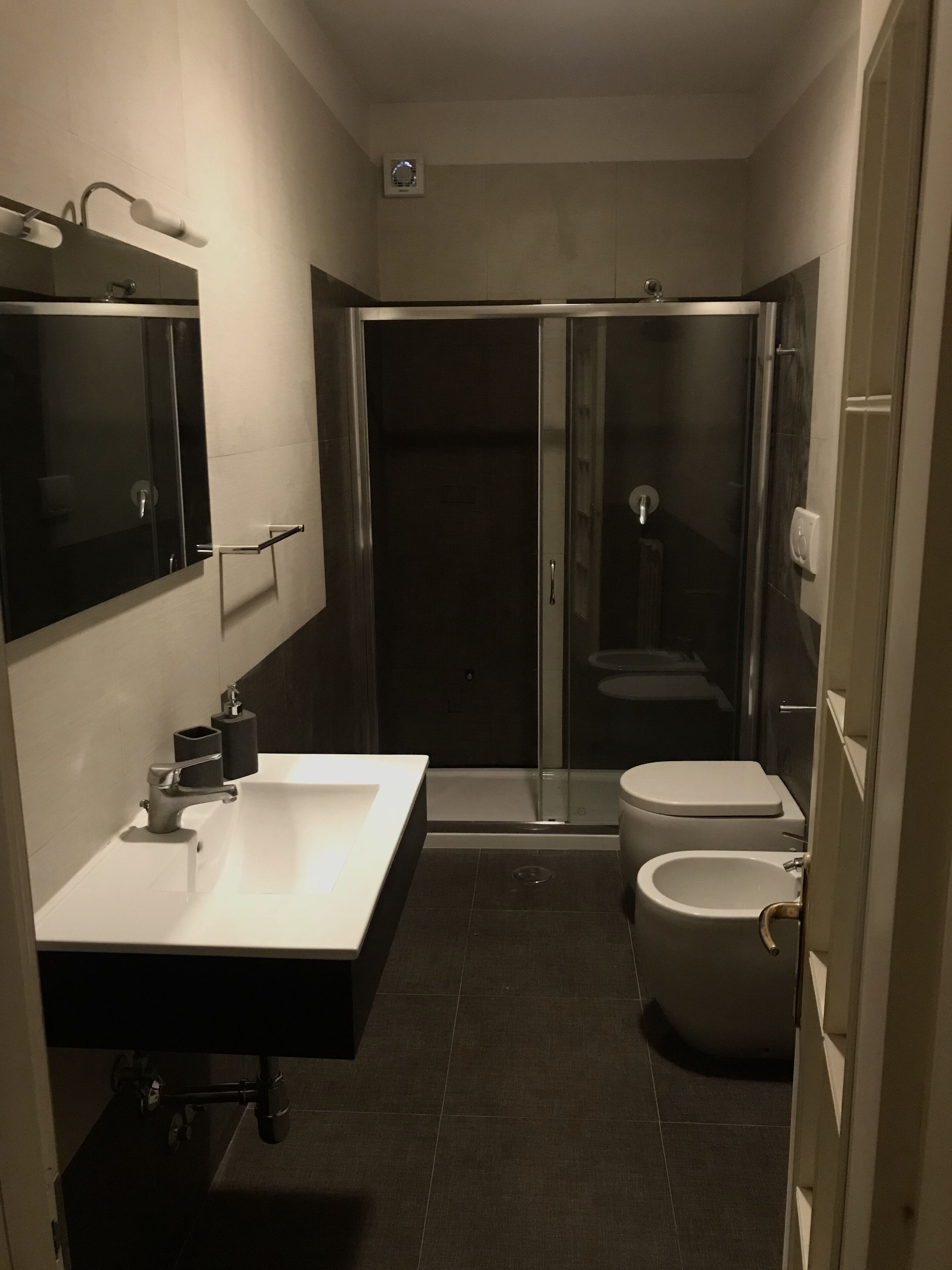 A modern bathroom with a glass-enclosed shower, a standalone toilet, and a sink with a mirror above it.