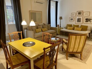 A living room with a yellow dining table, beige sofas, and a patterned rug.
