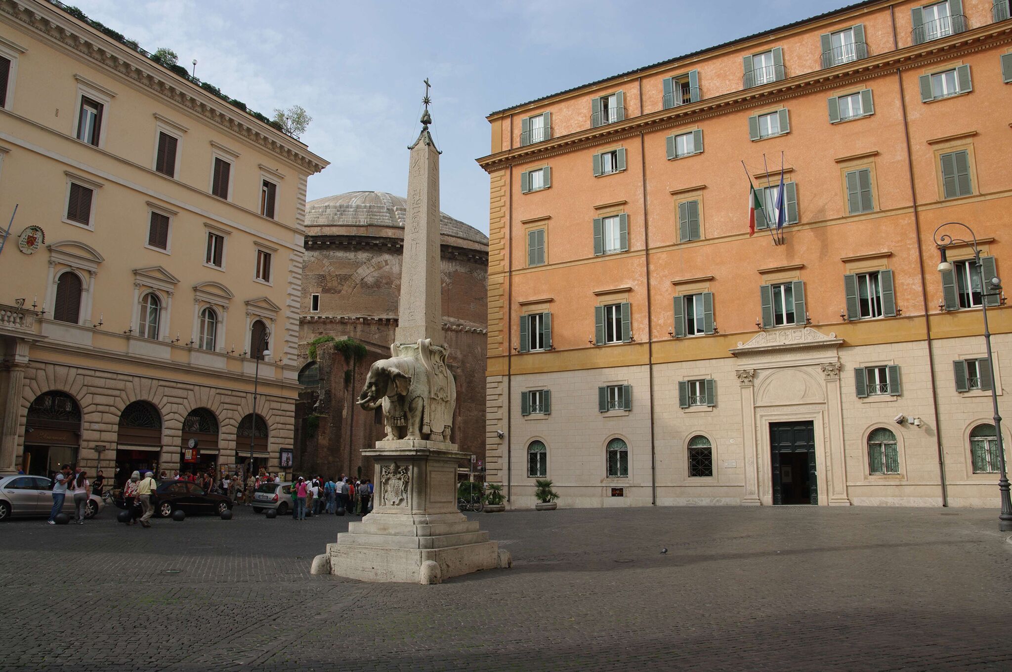 A public square with a central monument, surrounded by historic buildings with classical architecture.