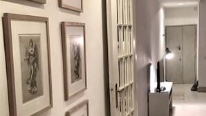 A hallway with framed artwork on the walls, a door with vertical bars, and a tiled floor. - Count Checco. A heaven in the rooftops of Rome few steps away from the pantheon (Roma)