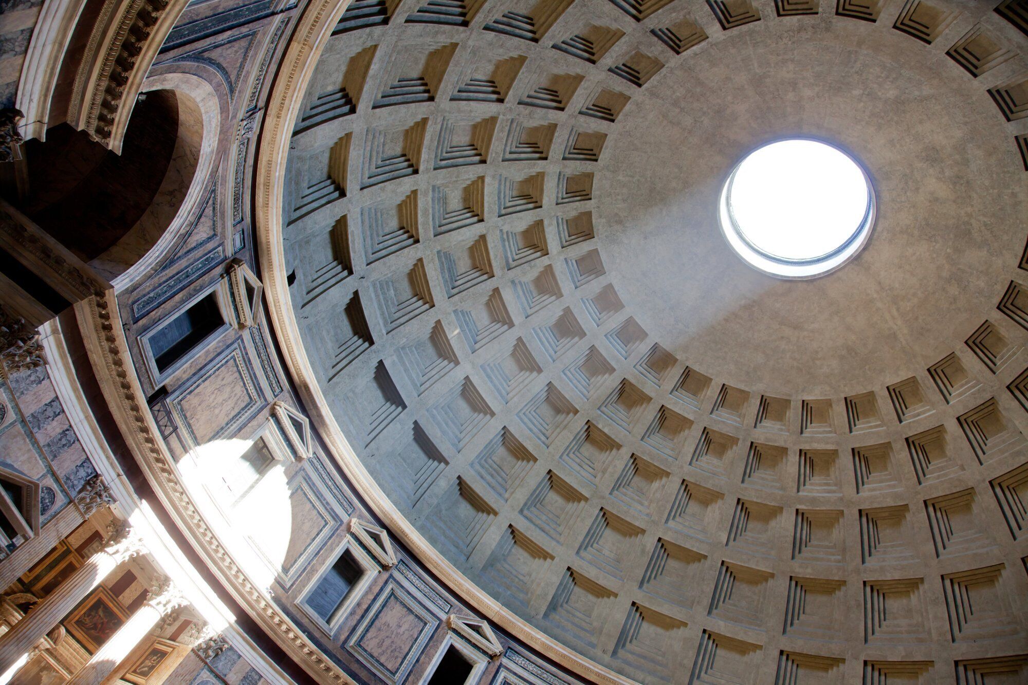Une vaste structure architecturale circulaire, dotée d’une verrière centrale et d’une conception symétrique comprenant plusieurs niveaux et une série d’ouvertures régulièrement espacées.