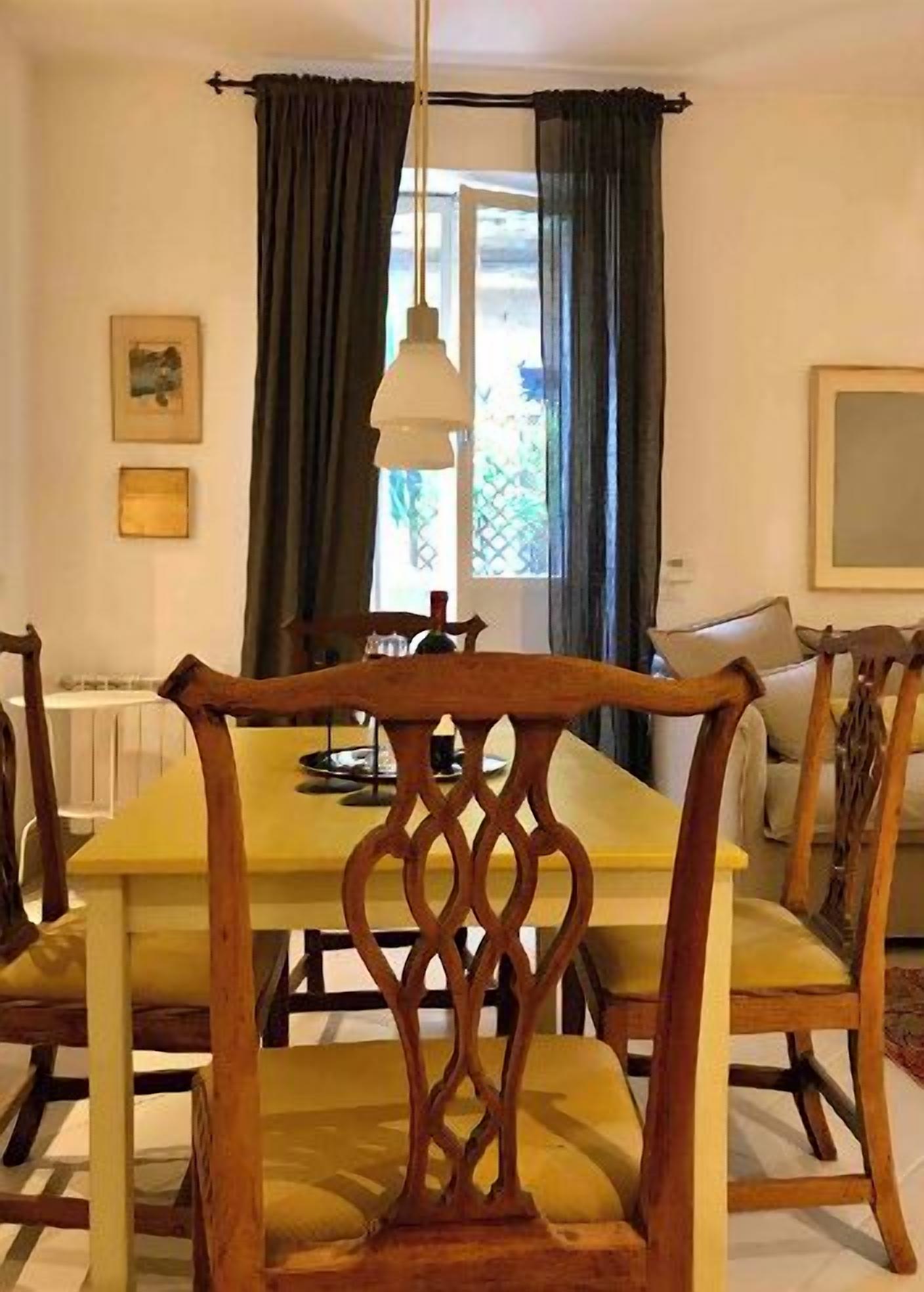 A dining area with a wooden table and chairs, a hanging lamp, and a window with curtains.