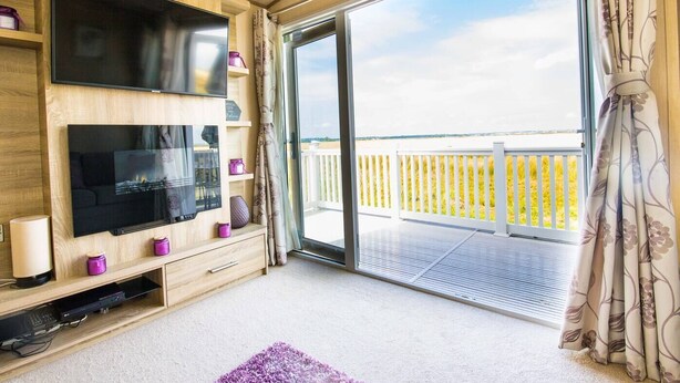 Un balcón con vista al mar, un televisor de pantalla plana en la pared y un mueble de madera con espacio de almacenamiento.