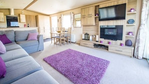 Una sala de estar moderna con un sofá gris, una alfombra morada, armarios de madera, un televisor y un comedor.