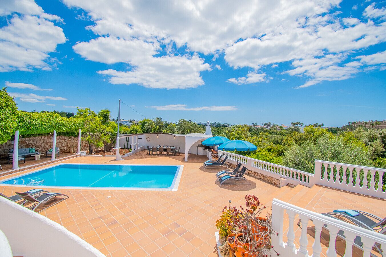 A rooftop pool area with a clear view of the surrounding landscape, a covered seating area, and a white railing.