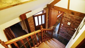 Una escalera de madera junto a un muro de ladrillo y una puerta que da a otra habitación.