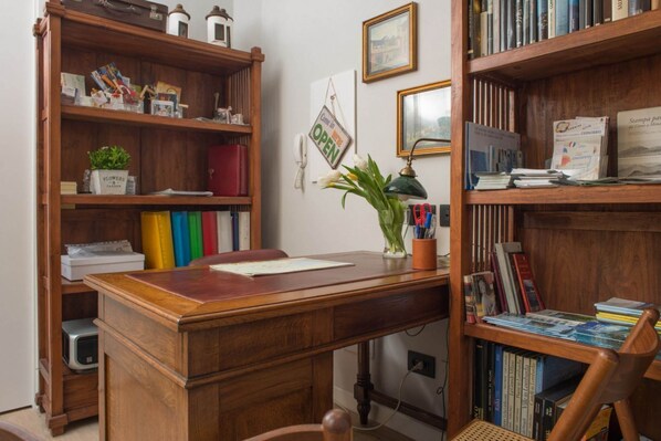 Un escritorio de madera con un jarrón de flores, un teléfono y un cartel que indica que la habitación está abierta.