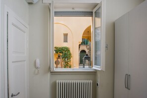A room with a window overlooking a courtyard, a radiator below the window, and a white door on the left.