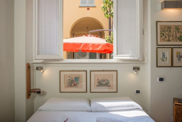 Quarto com cama, janela e impressões botânicas emolduradas na parede.