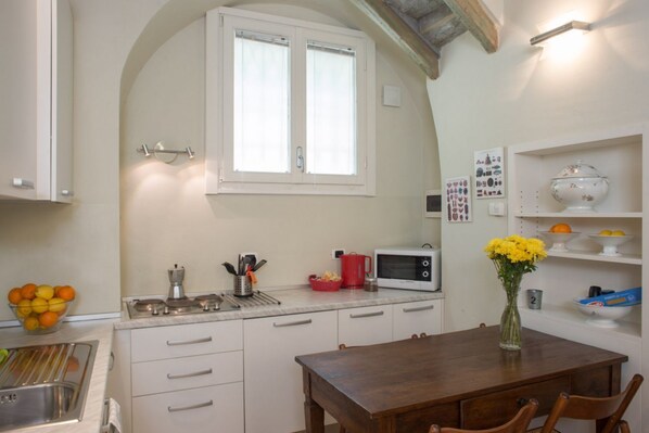 A kitchen with white cabinets, a wooden table, a microwave, and a vase with flowers.