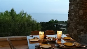 Ein Tisch ist für eine Mahlzeit auf einer Terrasse gedeckt, mit Blick auf das Meer.