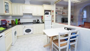 Une cuisine moderne avec des armoires blanches, un lave-linge encastré, un four à micro-ondes et un coin repas comprenant une table et des chaises.