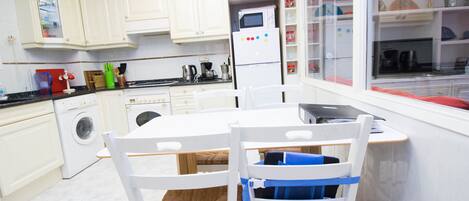 A modern kitchen with white cabinetry, a built-in oven, and a dining area with white chairs.