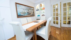Un coin repas avec une table en bois, des chaises blanches, un tableau au mur et une vitrine en verre contenant des assiettes.