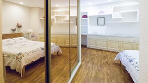 Une chambre avec un plancher en bois, un lit recouvert d’une couvre-lit à motifs floraux, une table de chevet avec une lampe et une commode.