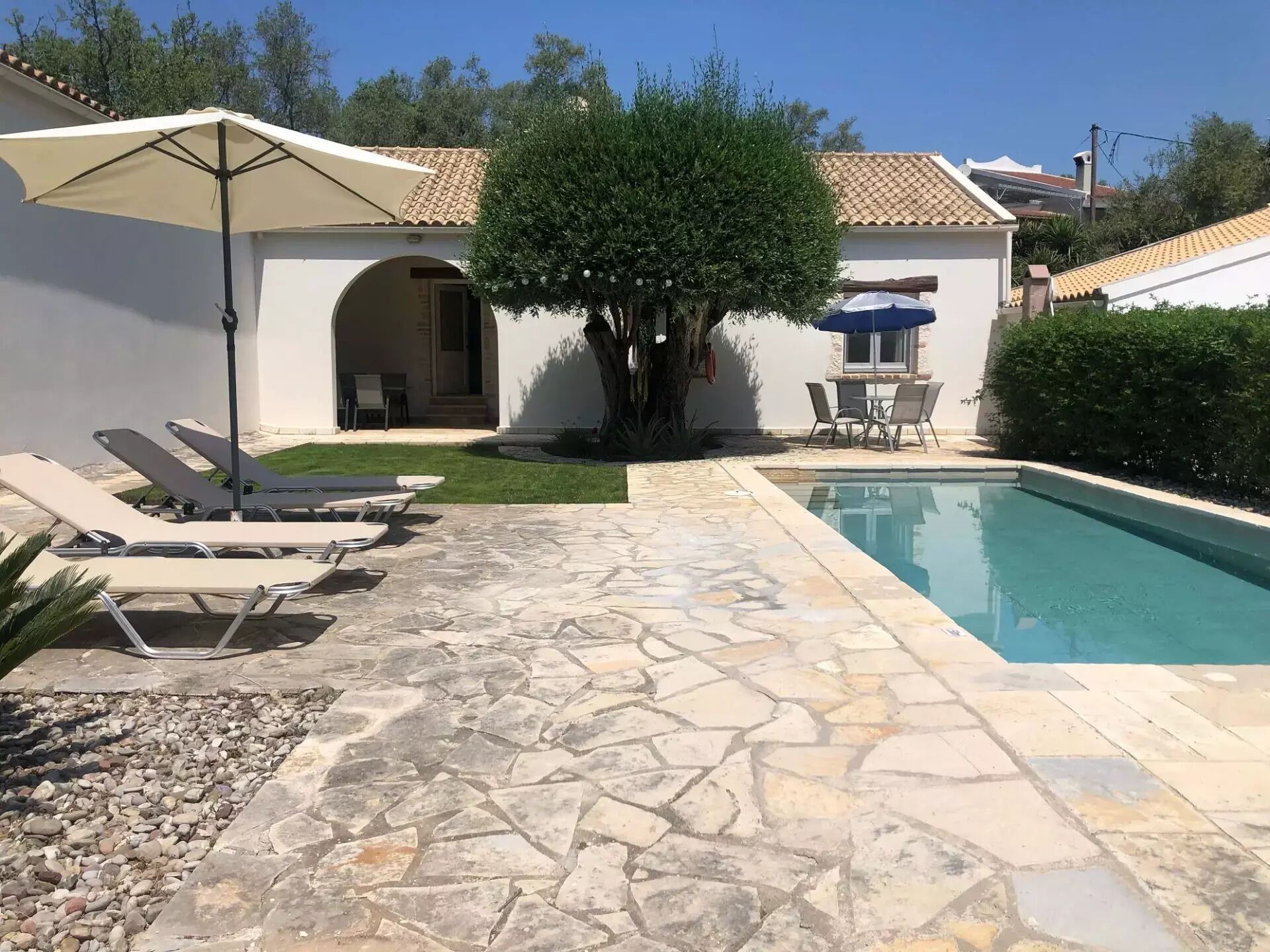 Ein Poolbereich mit Steinböden, Liegestühlen und Sonnenschirmen.