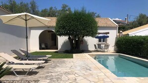 Ein Poolbereich mit Steinböden, Liegestühlen und Sonnenschirmen.