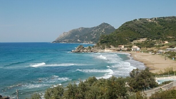 Eine Küstenlandschaft mit Strand, Felsformationen und einem Berg im Hintergrund.