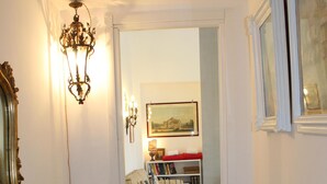 A hallway with a wooden table, a mirror, a chandelier, a sofa, a bookshelf, and a painting on the wall. - Naples city of the Sun and the Sea and 2500 years of history awaits you (Napoli)