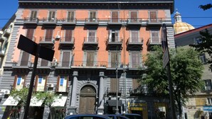 A multi-story building with a central entrance, balconies, and a dome structure in the background. - Naples city of the Sun and the Sea and 2500 years of history awaits you (Napoli)