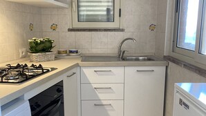 A compact kitchen with white cabinets, a built-in oven, a washing machine, and a refrigerator. - apartment/ flat - with a large terrace overlooking the sea (Taormina)
