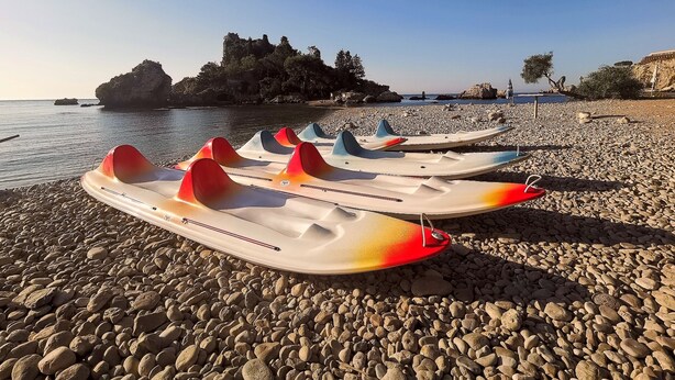 A row of colorful kayaks lined up on a pebble beach with a rocky island and clear sky in the background. - apartment/ flat - with a large terrace overlooking the sea (Taormina)