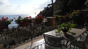 An outdoor patio with a table and chairs, overlooking a scenic view of the sea and a mountainous landscape. - apartment/ flat - with a large terrace overlooking the sea (Taormina)