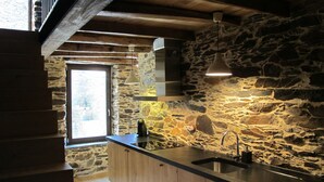 Eine Küche mit einer Steinwand, Holzschränken, einem Spülbecken und einer Treppe zu einer oberen Ebene.