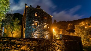 Ein Steinhaus mit vielen Fenstern, umgeben von Bäumen und einer Steinsäule.