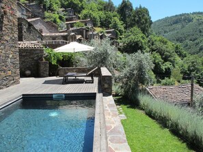 Una piscina con muros de piedra, un área de descanso con mesa y sillas, y vistas a un pueblo en la ladera.