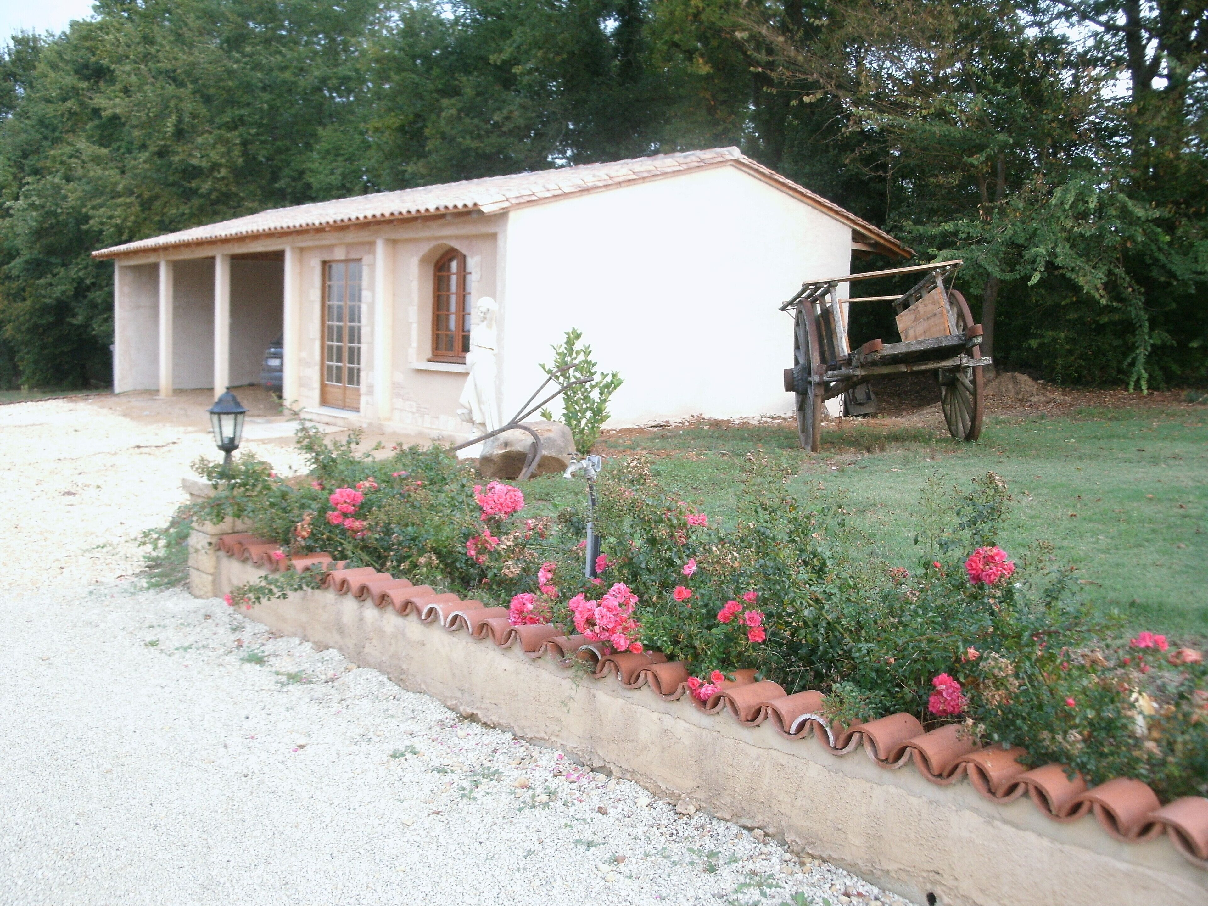 Un edificio rustico con tetto in tegole, un piccolo portico e un giardino con fiori rosa.