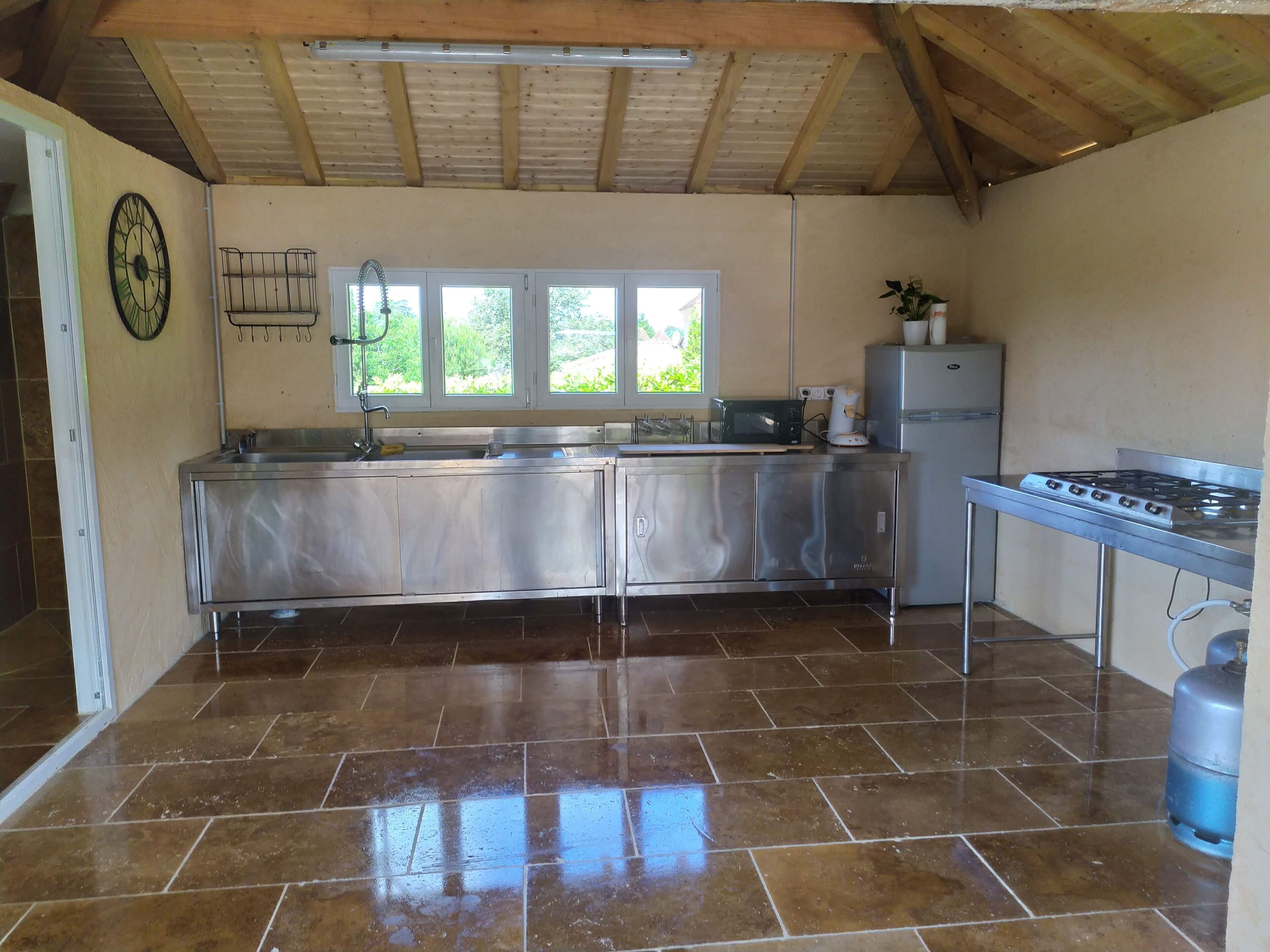 Cocina con electrodomésticos de acero inoxidable, piso de baldosas y ventana con vista a áreas verdes.