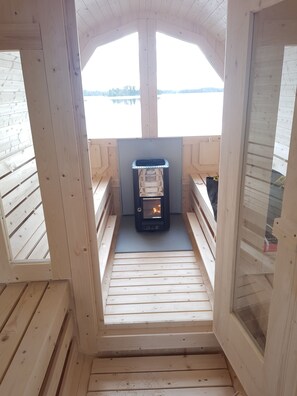 Eine Holzhütte mit einem zentralen Kamin, Holzbänken und Seeblick.