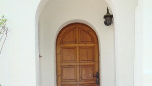 A wooden door with a white arched entrance, a potted plant with red flowers, and a wall-mounted light fixture.
