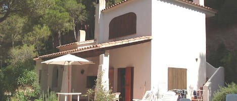 A white villa with a tiled roof, a covered patio area, and a pool.