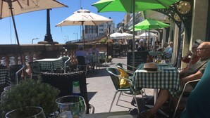 Un espace extérieur aménagé pour les repas, avec des tables, des chaises, des parasols et une vue sur la rue.