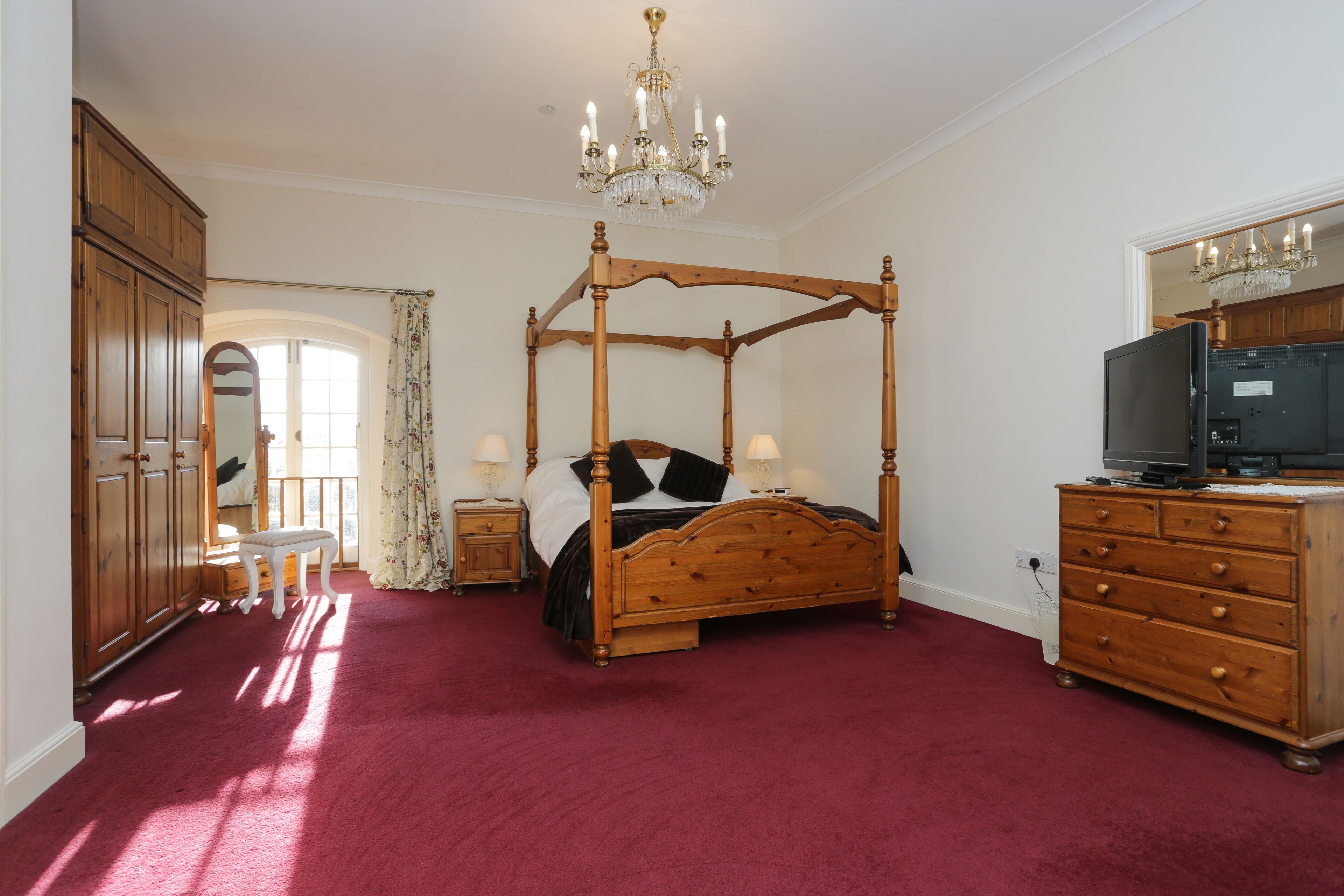 A bedroom with a four-poster bed, wooden dresser, and a television on a dresser.