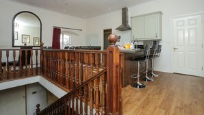 Une cuisine spacieuse avec un escalier en bois, un lustre et un coin repas agrémenté de tabourets de bar.